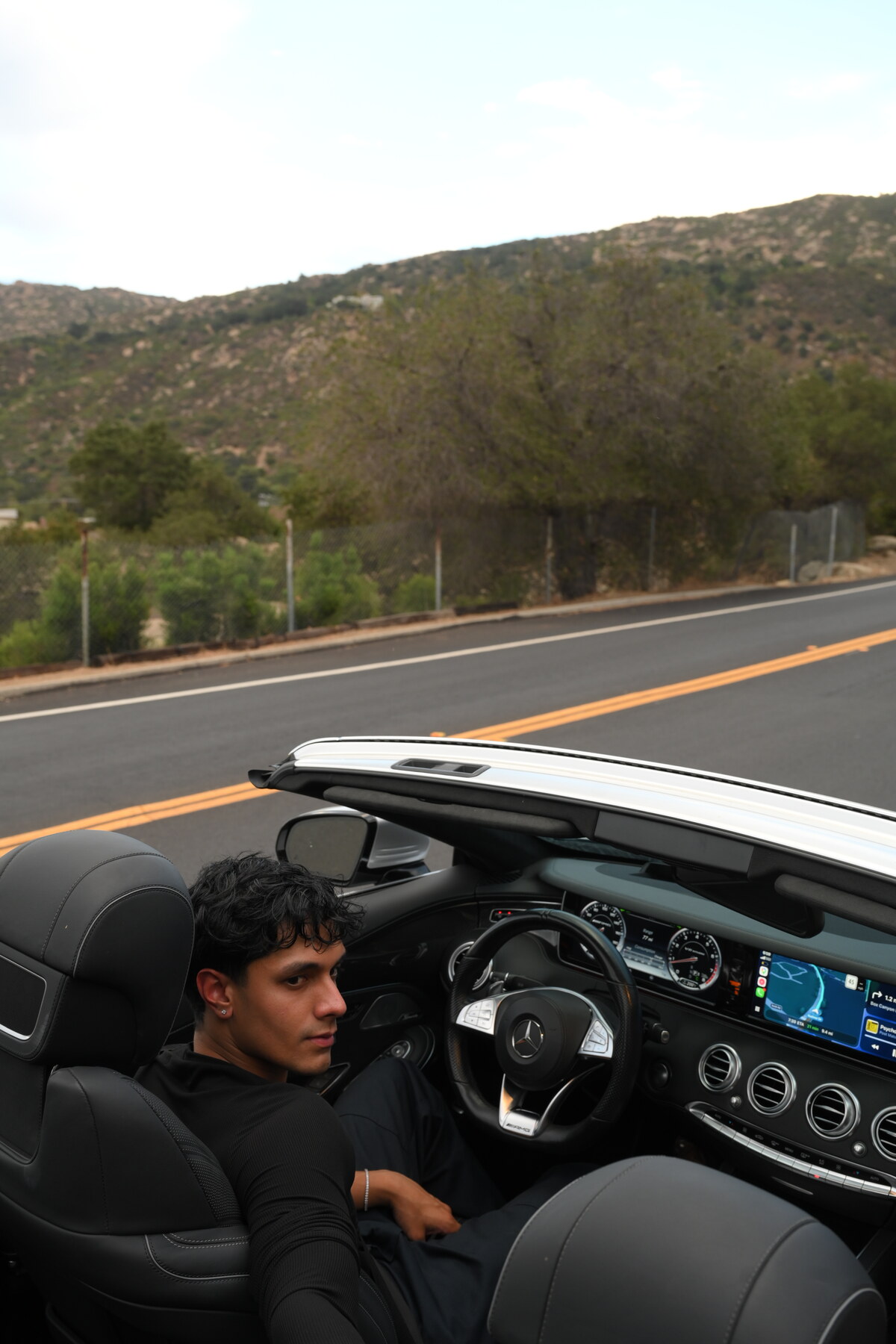 Aryan Mahajan seated in a black convertible on a California mountain road