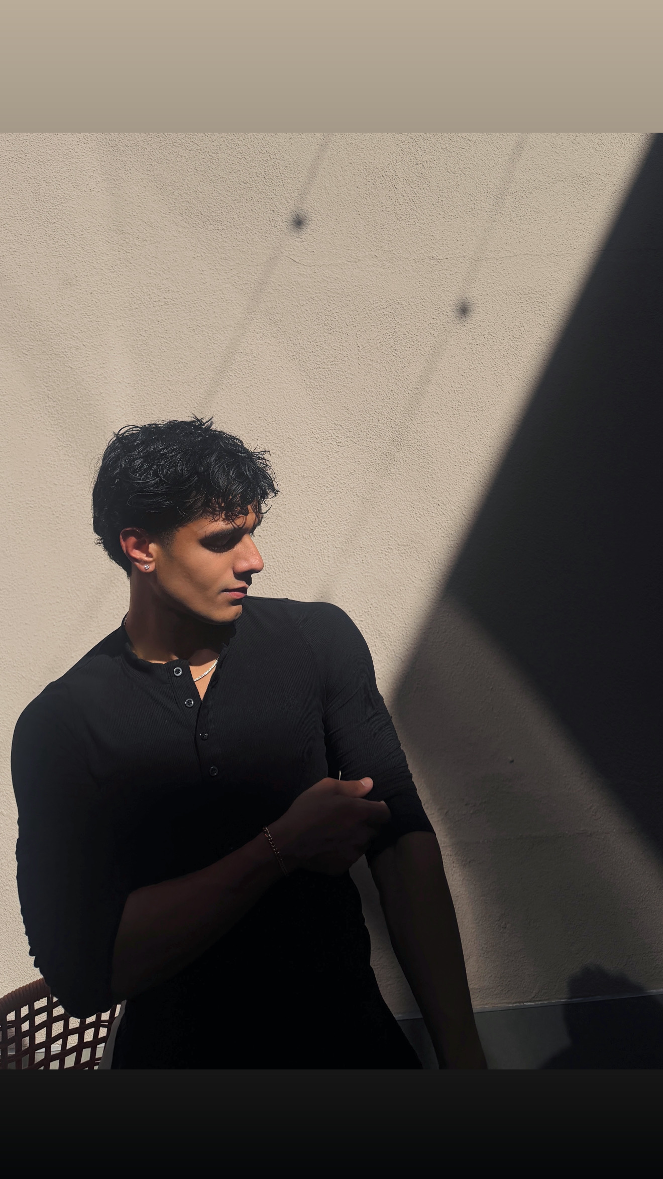 Aryan Mahajan in a black Henley beside a beige wall with a diagonal shadow