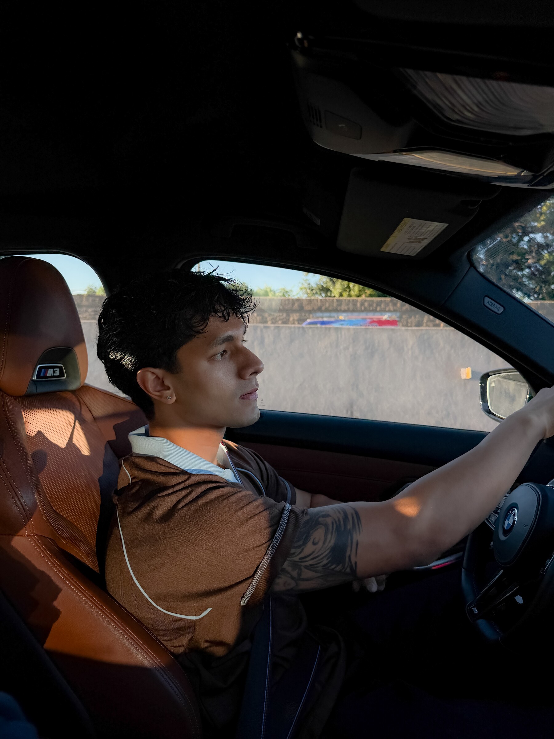 Aryan Mahajan wearing a brown jersey while driving a green BMW M3