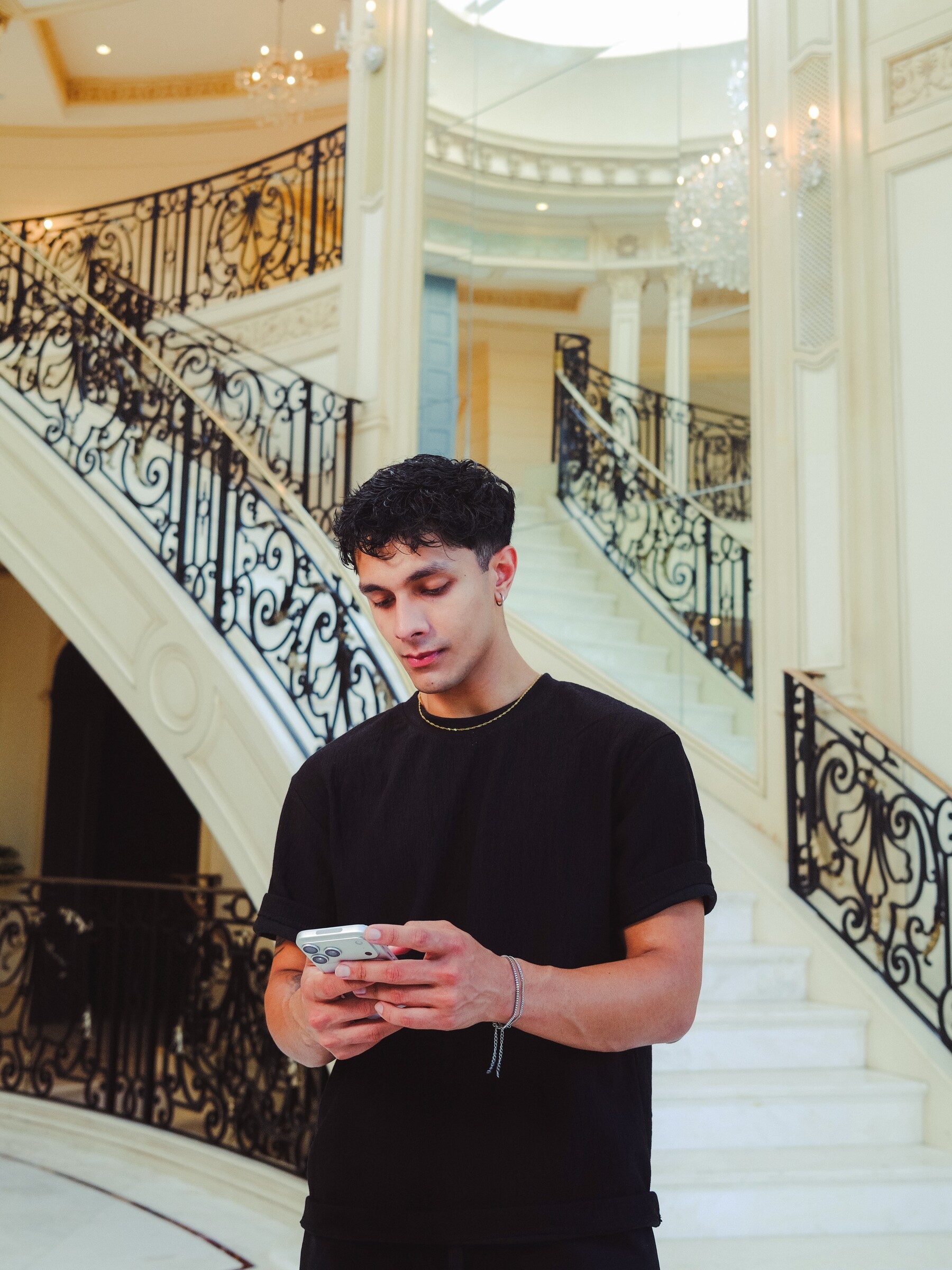 Aryan Mahajan checking his phone beside a grand staircase