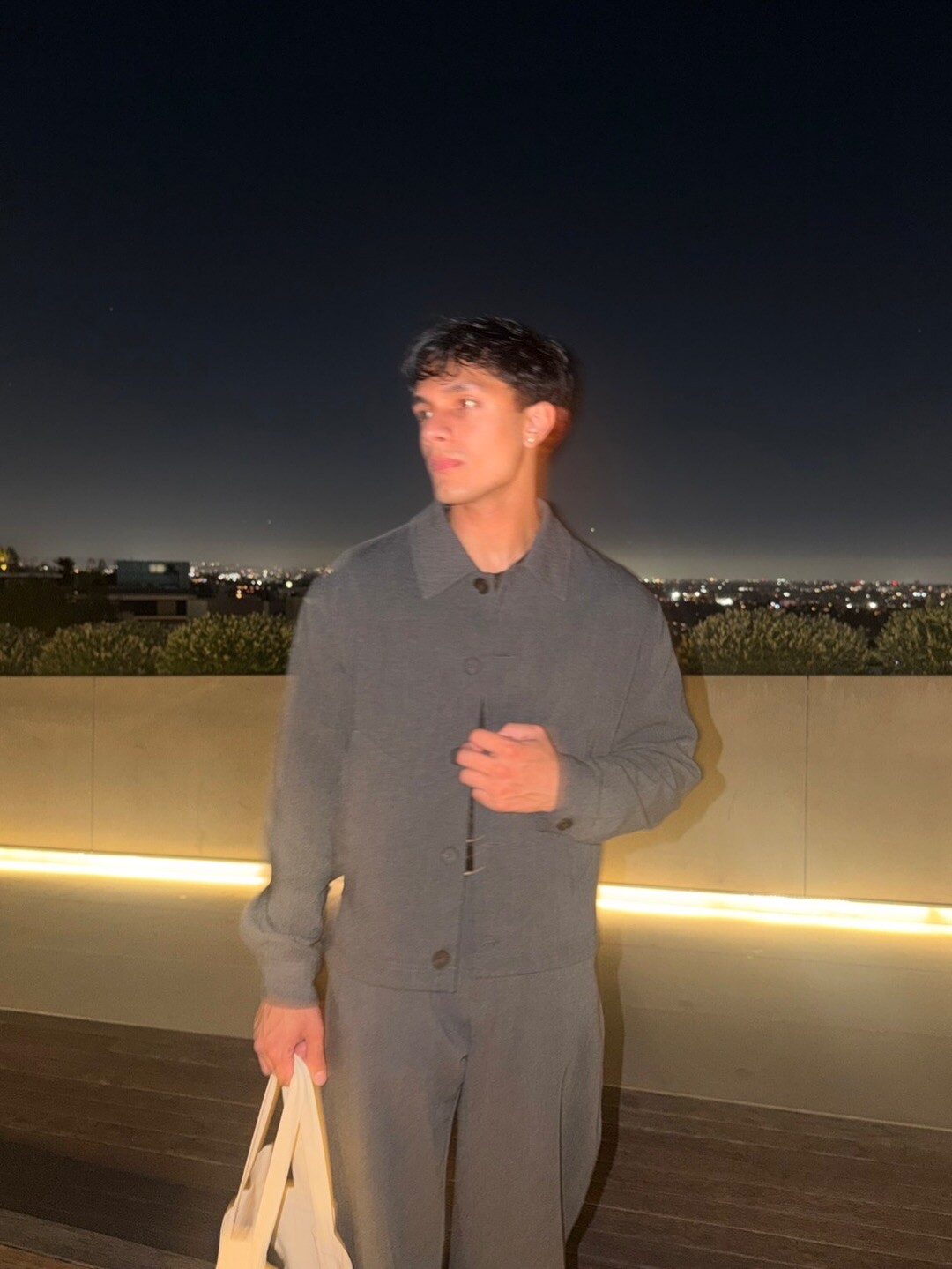 Aryan Mahajan wearing gray and carrying a tote on a terrace at night