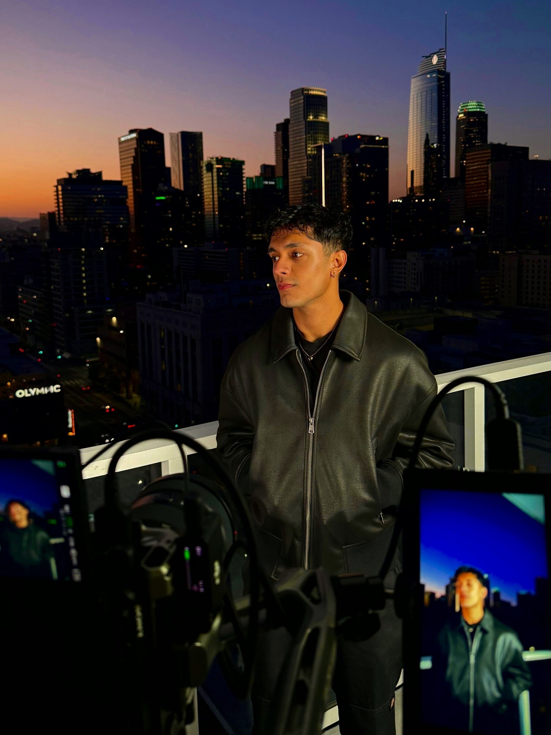 Aryan Mahajan wearing a black leather jacket beside the Los Angeles skyline at night