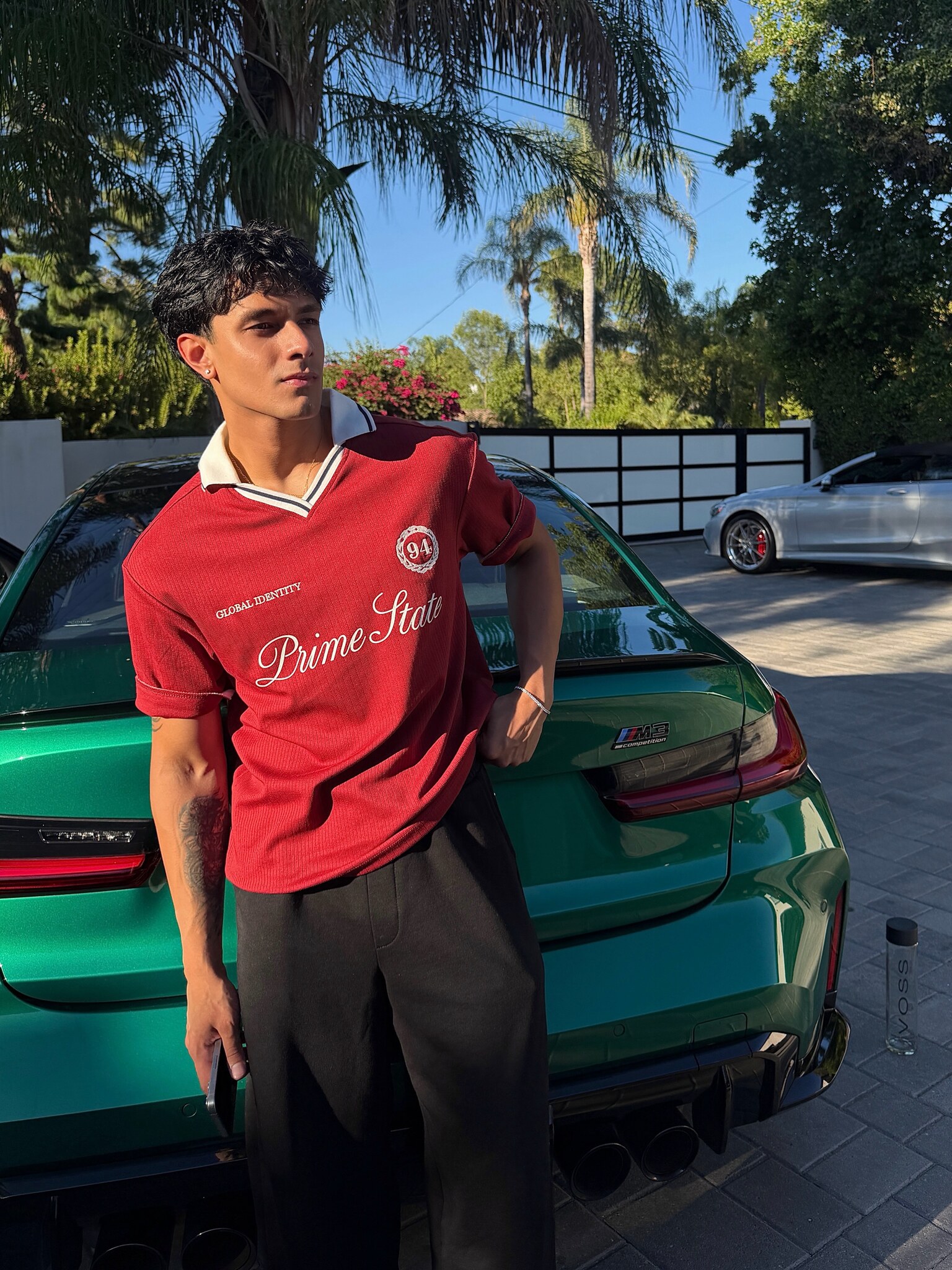 Aryan Mahajan wearing a red collared shirt beside a green BMW M3 in Los Angeles