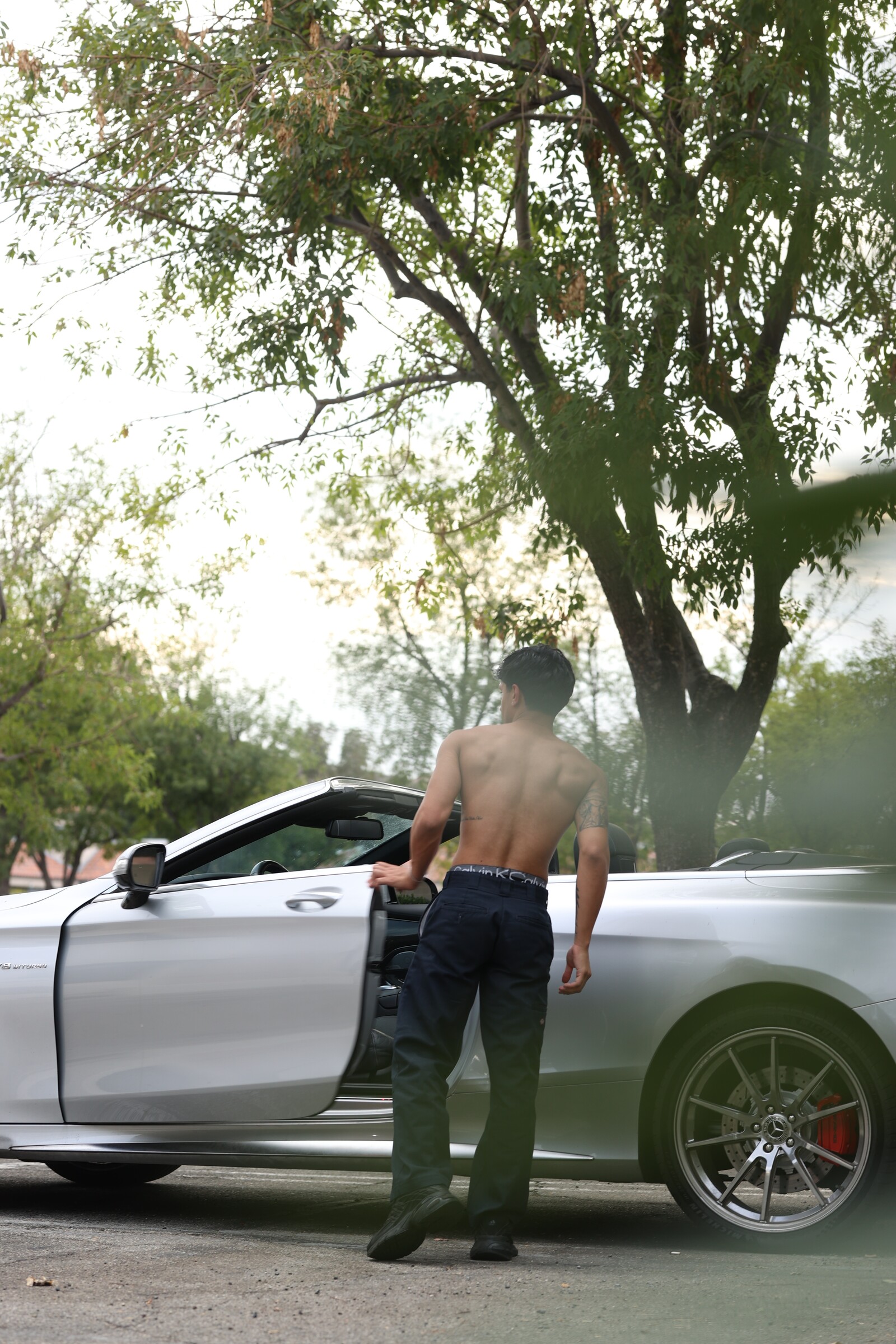 Aryan Mahajan standing shirtless beside a white Mercedes convertible
