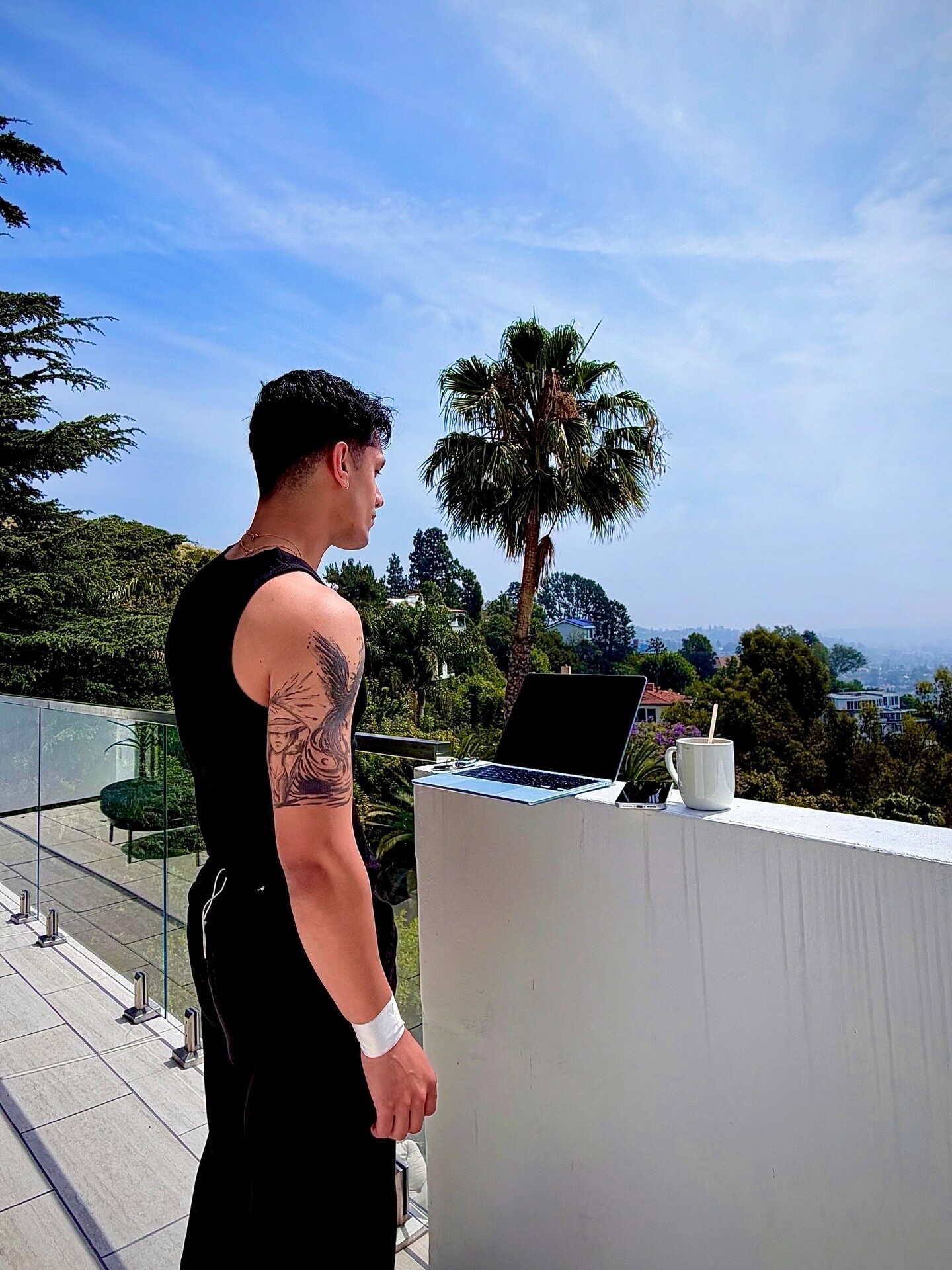 Aryan Mahajan beside a laptop and coffee on a terrace overlooking Los Angeles